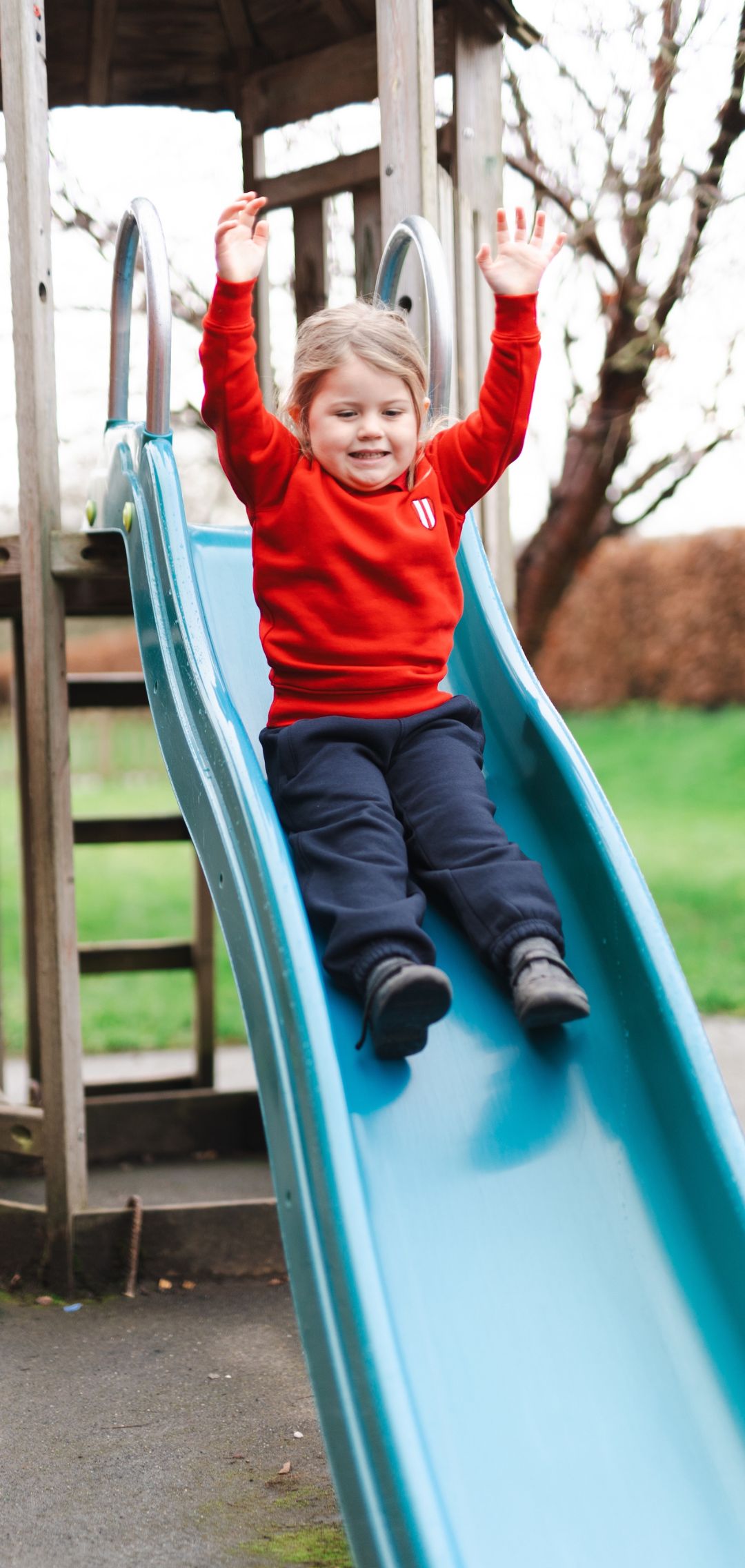 Nursery student going down slide with arms raised